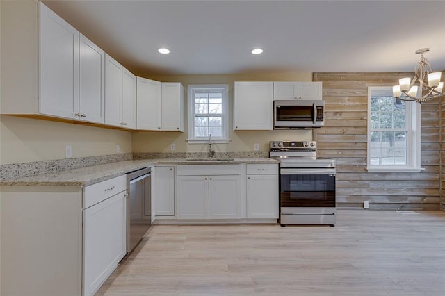 kitchen with appliances with stainless steel finishes, sink, white cabinetry, light hardwood / wood-style floors, and wooden walls