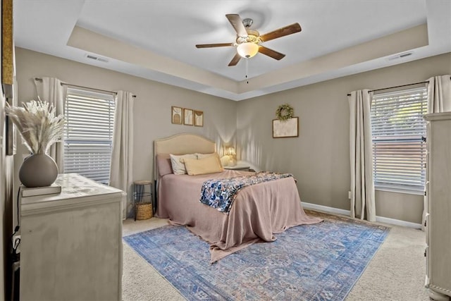 carpeted bedroom with ceiling fan and a tray ceiling