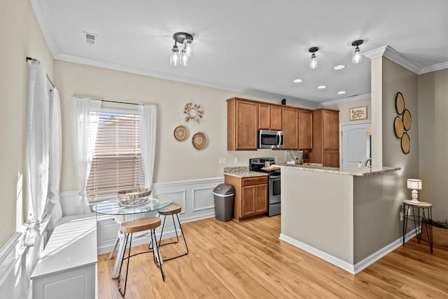 kitchen with kitchen peninsula, appliances with stainless steel finishes, light wood-type flooring, light stone counters, and ornamental molding