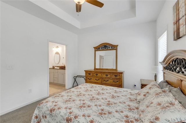 bedroom with ceiling fan, a tray ceiling, ensuite bathroom, and light carpet