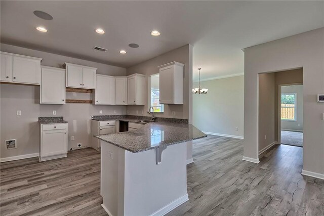 kitchen with kitchen peninsula, sink, light wood-type flooring, white cabinets, and stone counters