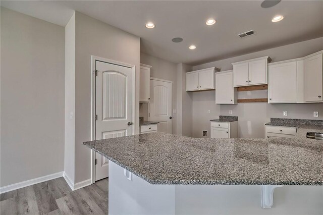 kitchen with white cabinetry, sink, light hardwood / wood-style flooring, a breakfast bar, and dark stone counters