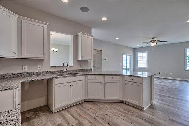 kitchen featuring kitchen peninsula, sink, light wood-type flooring, white cabinetry, and light stone counters