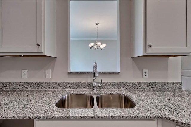 kitchen with a chandelier, white cabinetry, sink, ornamental molding, and light stone counters