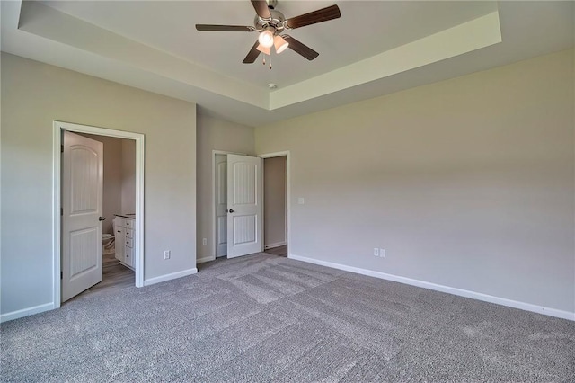 unfurnished bedroom featuring ceiling fan, ensuite bathroom, a raised ceiling, and carpet flooring