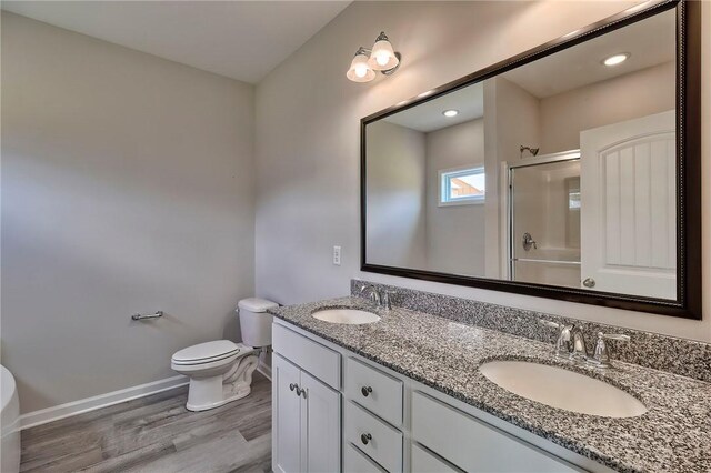 bathroom featuring wood-type flooring, a shower with door, toilet, and vanity