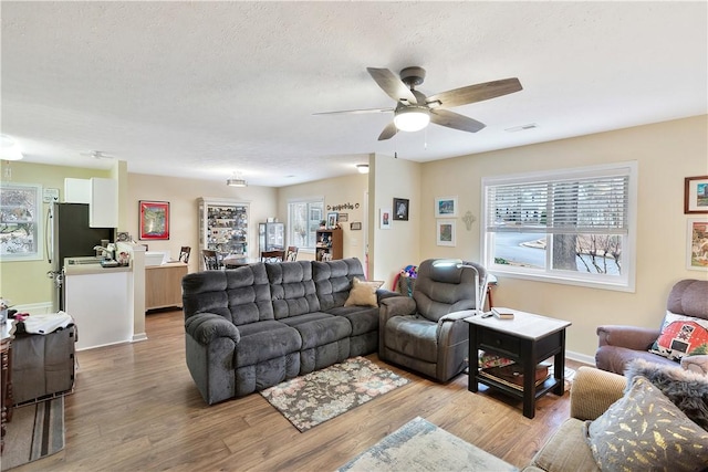 living room with ceiling fan, a textured ceiling, and light hardwood / wood-style flooring