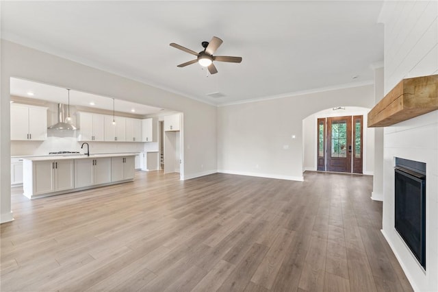 unfurnished living room with ceiling fan, sink, light hardwood / wood-style flooring, and crown molding