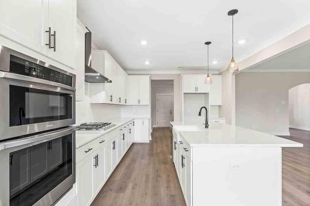 kitchen featuring pendant lighting, appliances with stainless steel finishes, white cabinetry, an island with sink, and light wood-type flooring