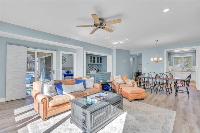 living room with sink, ceiling fan with notable chandelier, and light hardwood / wood-style flooring