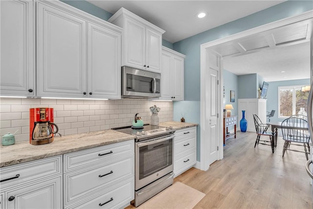 kitchen featuring white cabinets, appliances with stainless steel finishes, backsplash, light stone counters, and light hardwood / wood-style flooring