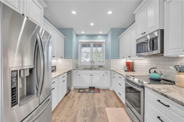 kitchen with white cabinetry, sink, light hardwood / wood-style flooring, backsplash, and stainless steel appliances