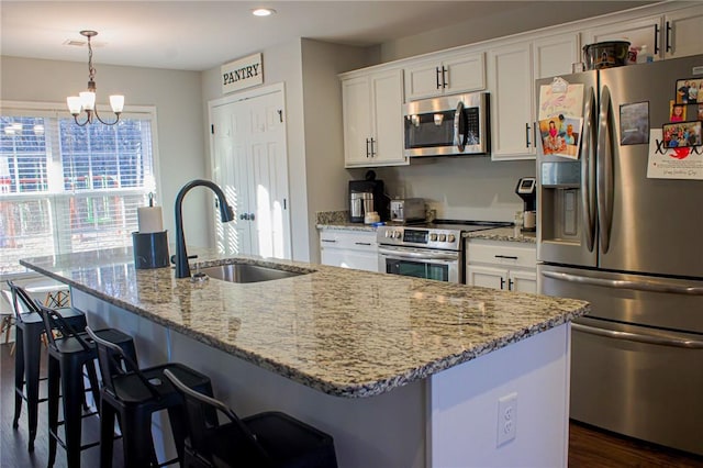 kitchen featuring hanging light fixtures, sink, white cabinets, a center island with sink, and stainless steel appliances