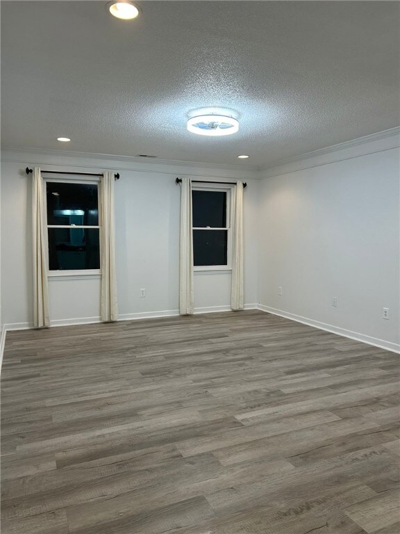 empty room with baseboards, a textured ceiling, ornamental molding, and wood finished floors