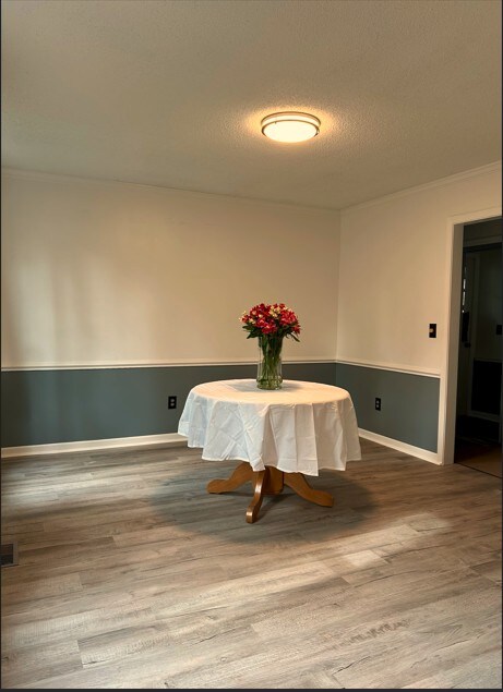 unfurnished dining area featuring a textured ceiling, baseboards, wood finished floors, and crown molding