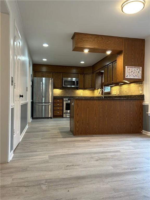 kitchen with dark countertops, light wood-style floors, tasteful backsplash, and appliances with stainless steel finishes