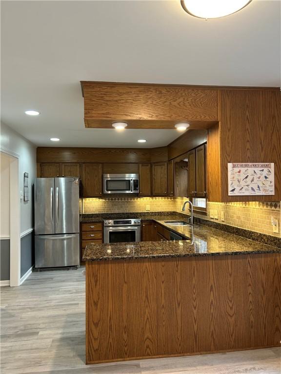 kitchen featuring dark stone counters, appliances with stainless steel finishes, a peninsula, a sink, and backsplash