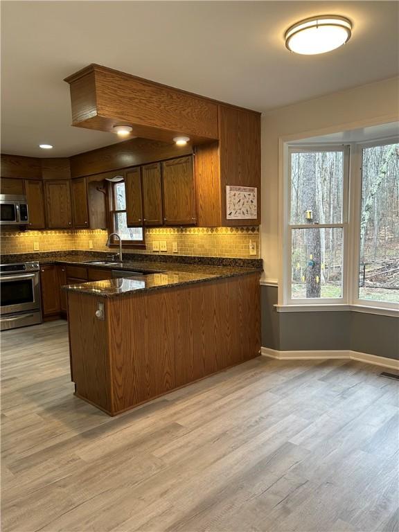 kitchen featuring appliances with stainless steel finishes, light wood-style floors, a peninsula, and tasteful backsplash