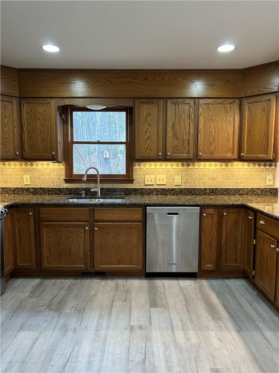 kitchen featuring a sink, light wood finished floors, backsplash, and stainless steel dishwasher