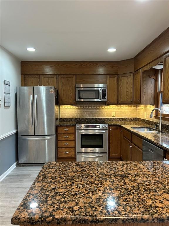 kitchen with appliances with stainless steel finishes, backsplash, a sink, and dark stone counters