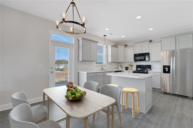 kitchen featuring sink, decorative light fixtures, a center island, light hardwood / wood-style flooring, and black appliances