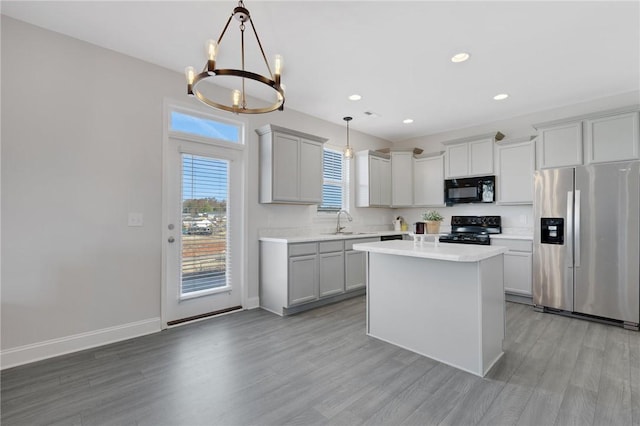 kitchen with pendant lighting, sink, a center island, black appliances, and light hardwood / wood-style flooring