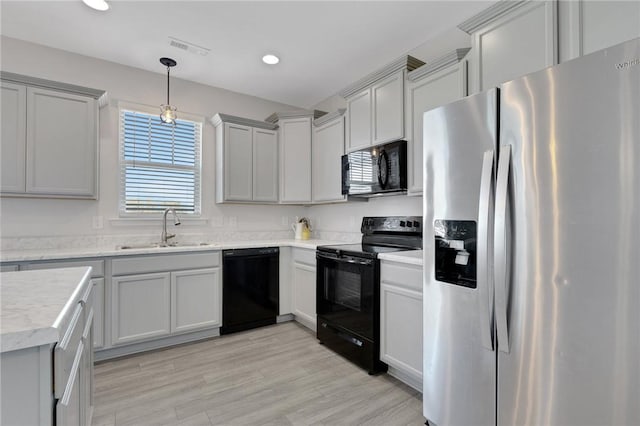 kitchen with hanging light fixtures, sink, light wood-type flooring, and black appliances