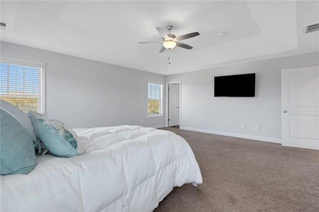 bedroom with multiple windows, ceiling fan, a tray ceiling, and carpet