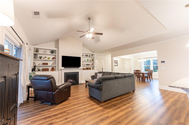 living room featuring hardwood / wood-style flooring, vaulted ceiling, ceiling fan with notable chandelier, and built in features