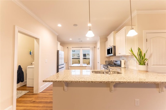 kitchen featuring appliances with stainless steel finishes, a breakfast bar, white cabinets, hanging light fixtures, and crown molding