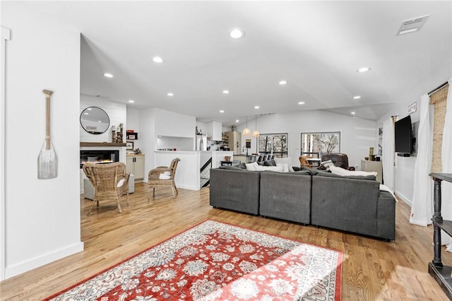 living area featuring recessed lighting, visible vents, a glass covered fireplace, and light wood-style flooring