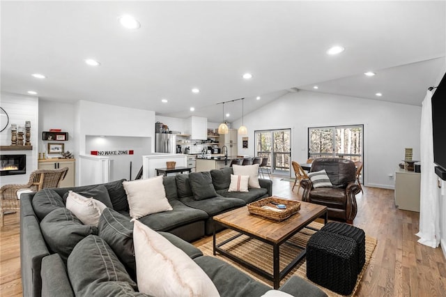living room with recessed lighting, a glass covered fireplace, light wood finished floors, and lofted ceiling