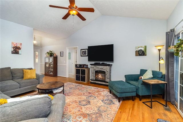 living room featuring lofted ceiling, hardwood / wood-style flooring, a stone fireplace, and ceiling fan