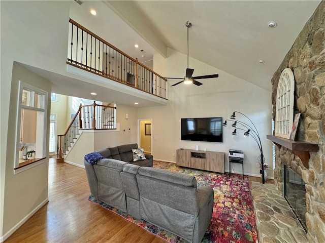 living room featuring wood-type flooring, high vaulted ceiling, a fireplace, and beam ceiling