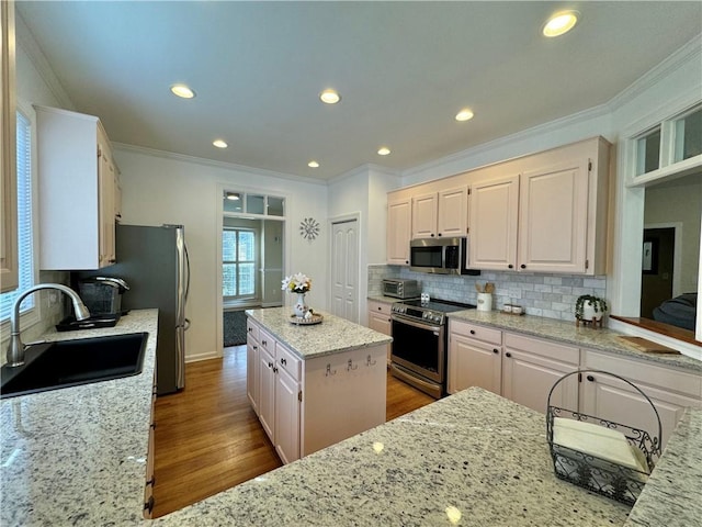 kitchen with sink, stainless steel appliances, a center island, light stone countertops, and white cabinets