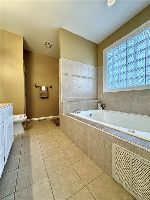 bathroom with tile patterned flooring, vanity, tiled tub, and toilet