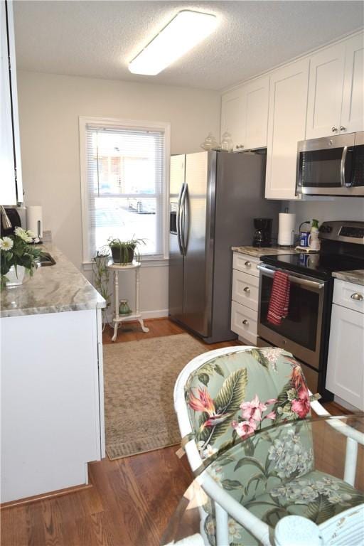 kitchen featuring white cabinetry, stainless steel appliances, wood-type flooring, and a textured ceiling