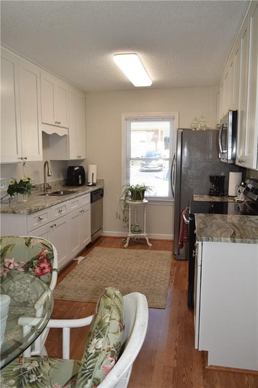 kitchen with sink, wood-type flooring, appliances with stainless steel finishes, light stone countertops, and white cabinets