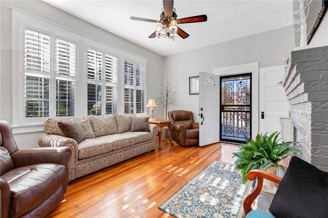 living room featuring wood-type flooring, plenty of natural light, a stone fireplace, and ceiling fan