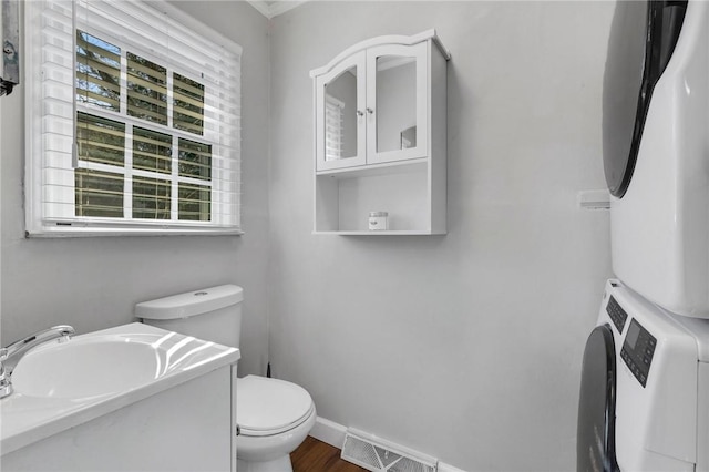 bathroom featuring stacked washer / dryer, vanity, wood-type flooring, and toilet