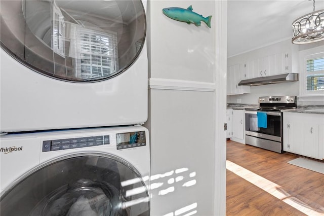 laundry area featuring ornamental molding, stacked washer and clothes dryer, and light hardwood / wood-style floors