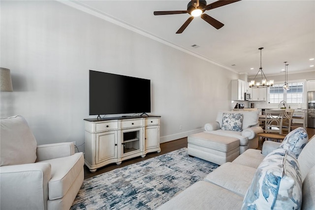 living room with ceiling fan with notable chandelier, ornamental molding, and dark hardwood / wood-style floors