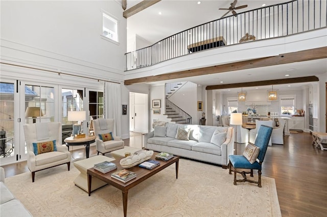 living room with beamed ceiling, wood-type flooring, a towering ceiling, and ceiling fan