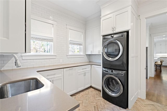 clothes washing area featuring sink, crown molding, stacked washing maching and dryer, cabinets, and light parquet flooring