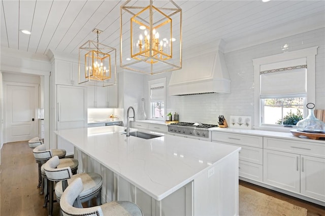 kitchen with a center island with sink, pendant lighting, custom range hood, and sink