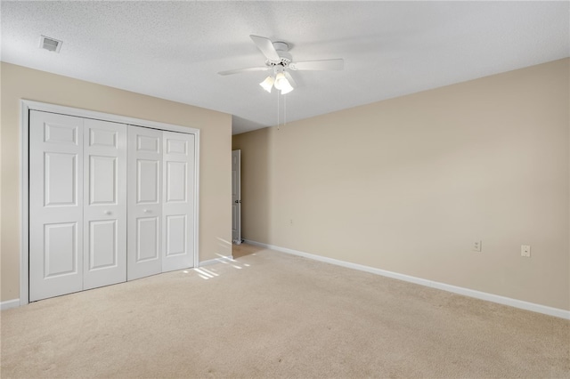 unfurnished bedroom featuring ceiling fan, light colored carpet, a closet, and a textured ceiling