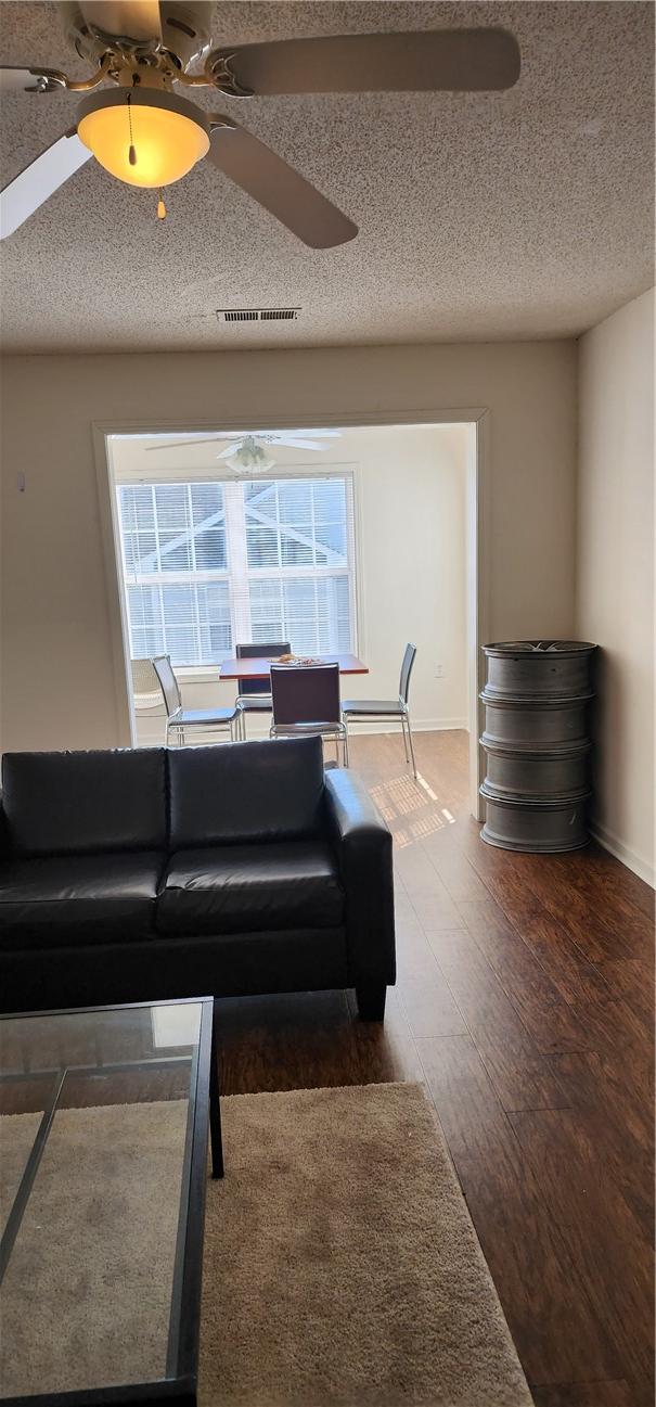 living room featuring a healthy amount of sunlight, ceiling fan, dark wood-type flooring, and a textured ceiling