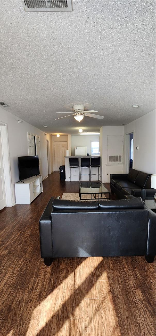 living room featuring dark wood-type flooring, ceiling fan, and a textured ceiling