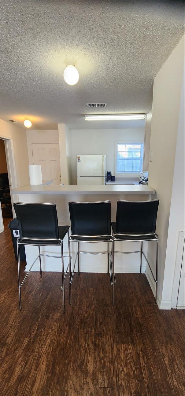 kitchen featuring a breakfast bar area, dark hardwood / wood-style flooring, white fridge, kitchen peninsula, and a textured ceiling