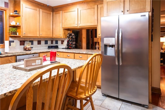 kitchen with light stone counters, decorative backsplash, stainless steel appliances, and a kitchen bar